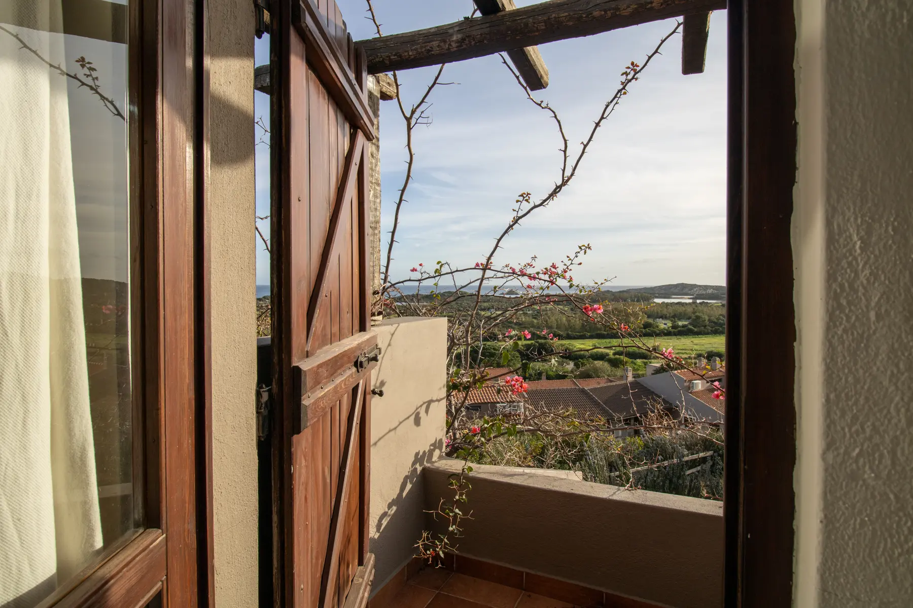 Porta in legno aperta su un terrazzino con bouganville